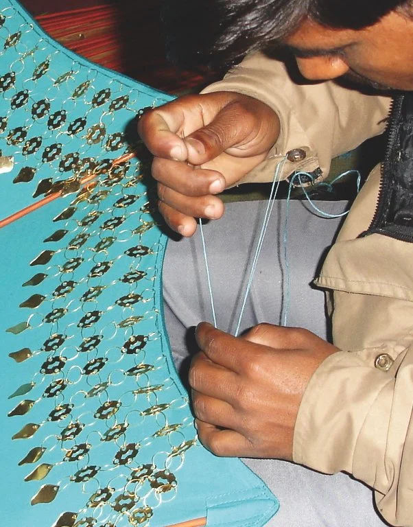 Close-up of an artisan hand-stitching mirrored and metal trim onto an Indian Garden Company Raj umbrella in Kerala, India.