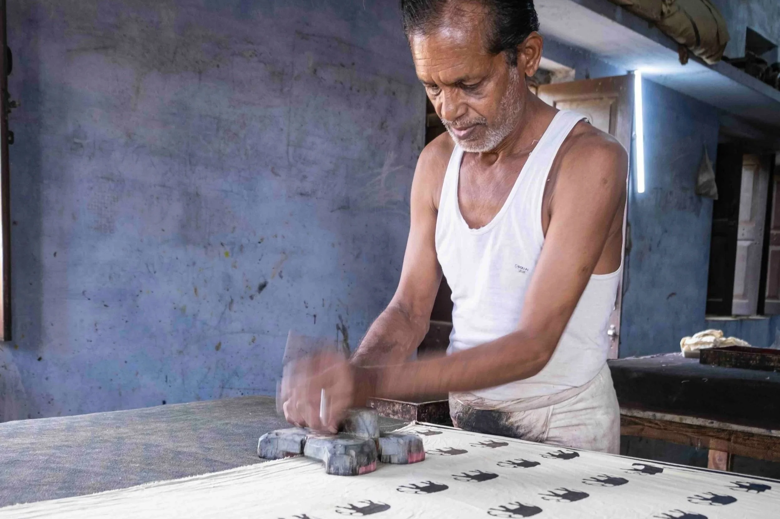 Artisan hand block printing a repeating pattern onto fabric in a traditional workshop in Bagru, Rajasthan