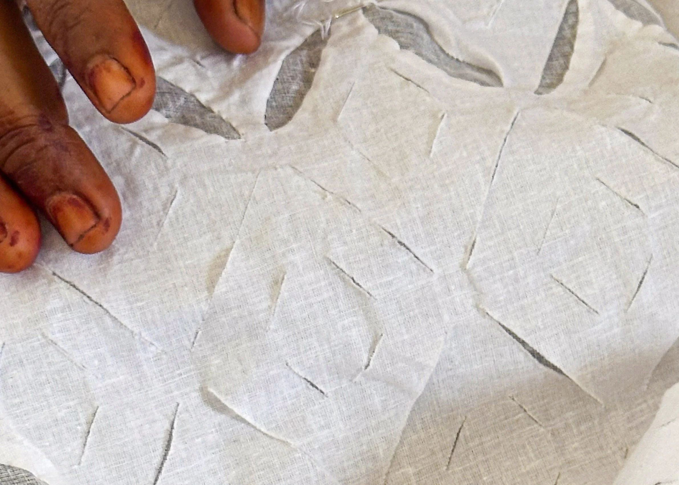 Close up of artisan’s hand on white handwoven cotton showing traditional kataab cutwork pattern, Bhangta, Barmer, Rajasthan