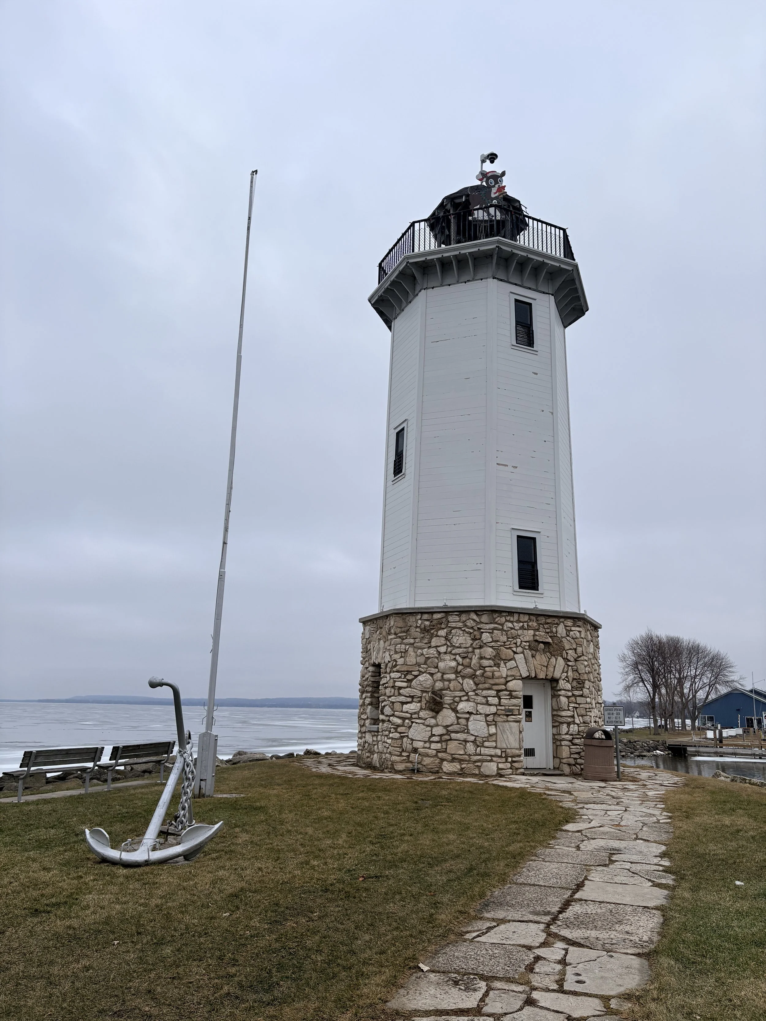 White lighthouse by the water with anchor sculpture and pathway, symbolizing Christ’s guidance and steady support for families.
