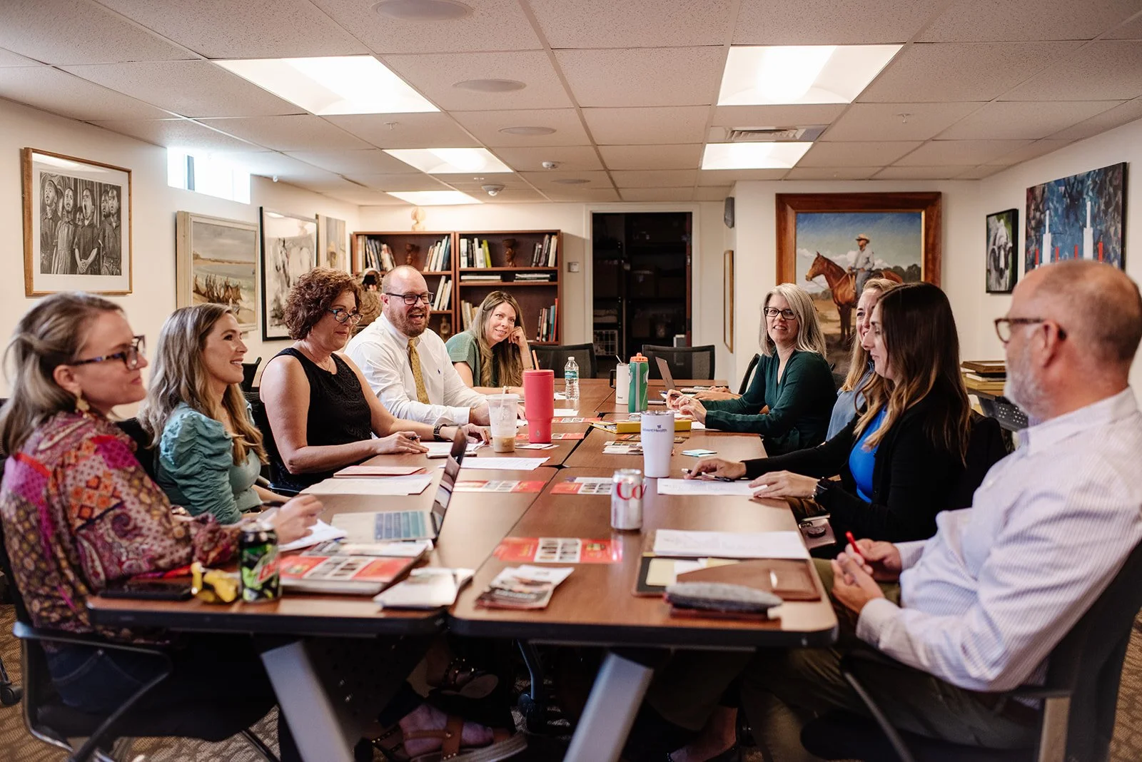 People working on ceramic pottery projects at a table in a classroom or workshop, with clay, bowls, and tools spread out.