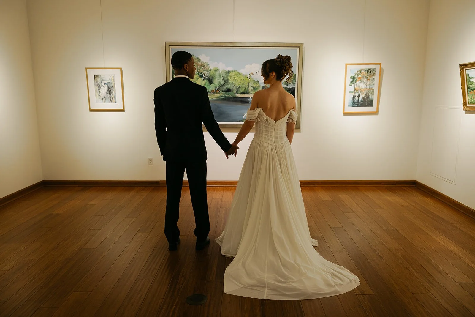 A couple in wedding attire holding hands and viewing artwork in an art gallery.