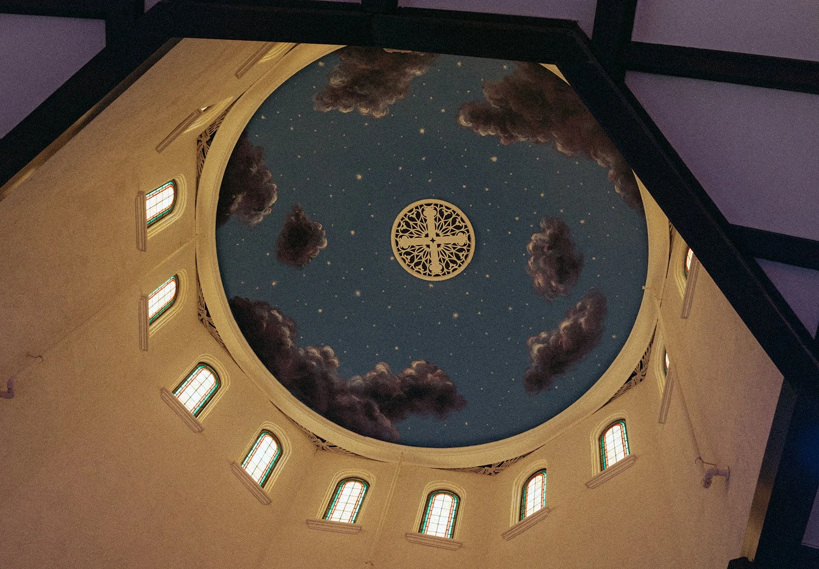 The ceiling of a church with a painted sky scene, including stars, clouds, and a decorative religious symbol in the center.