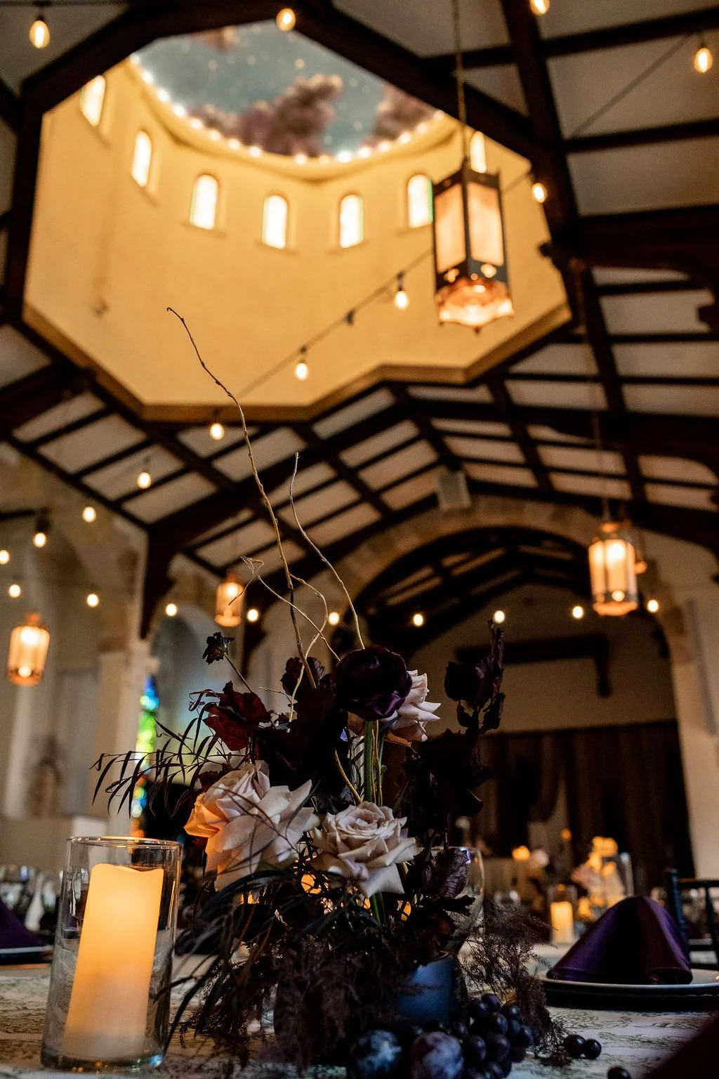 Interior of a decorated event space with a floral centerpiece, candles, and hanging lanterns.