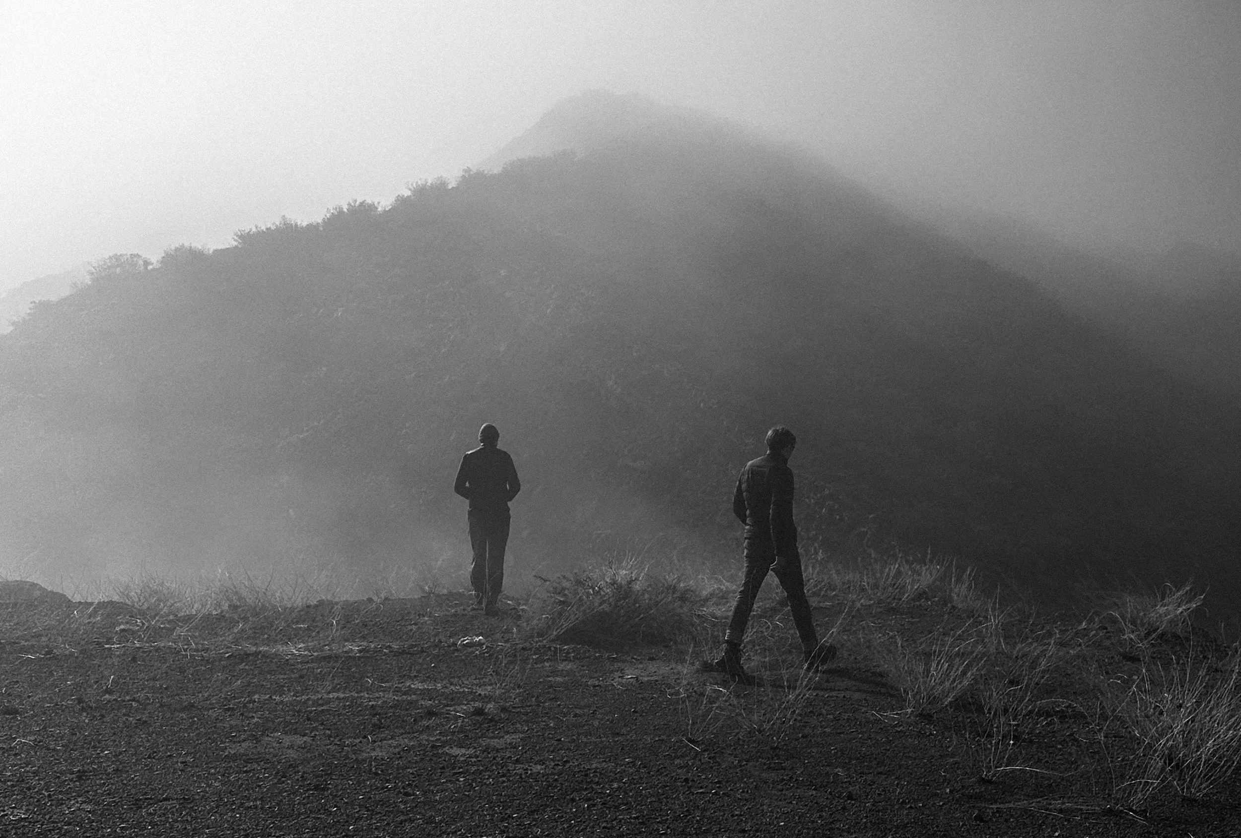 Milton Monsalvo y su socio Simon Rearte en un campo con montañas en la distancia y neblina, en blanco y negro.