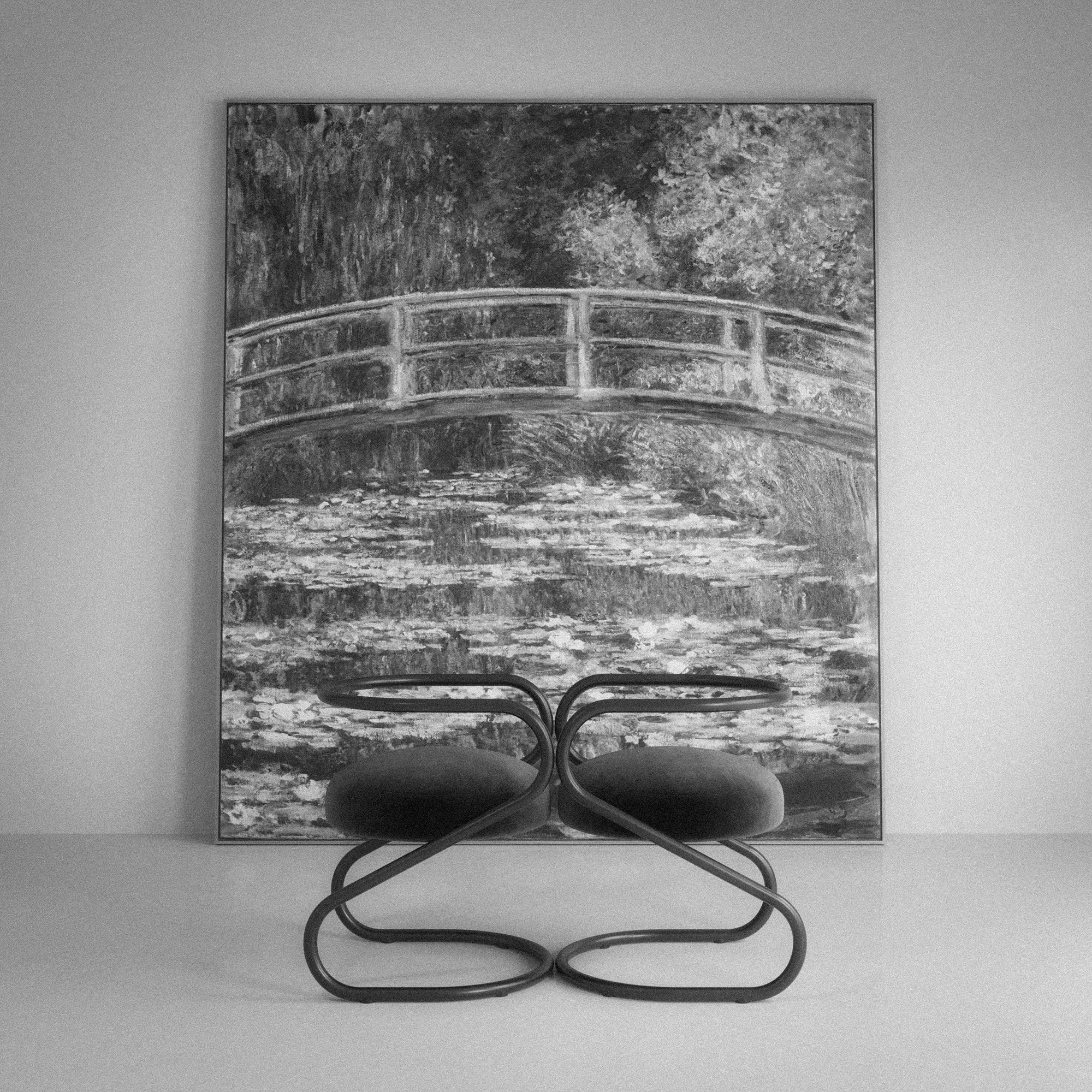 Fotografía en blanco y negro de dos SILLA S de diseño MONSALVO con estructura tubular curva, exhibida frente a una obra gráfica de Claude Monet