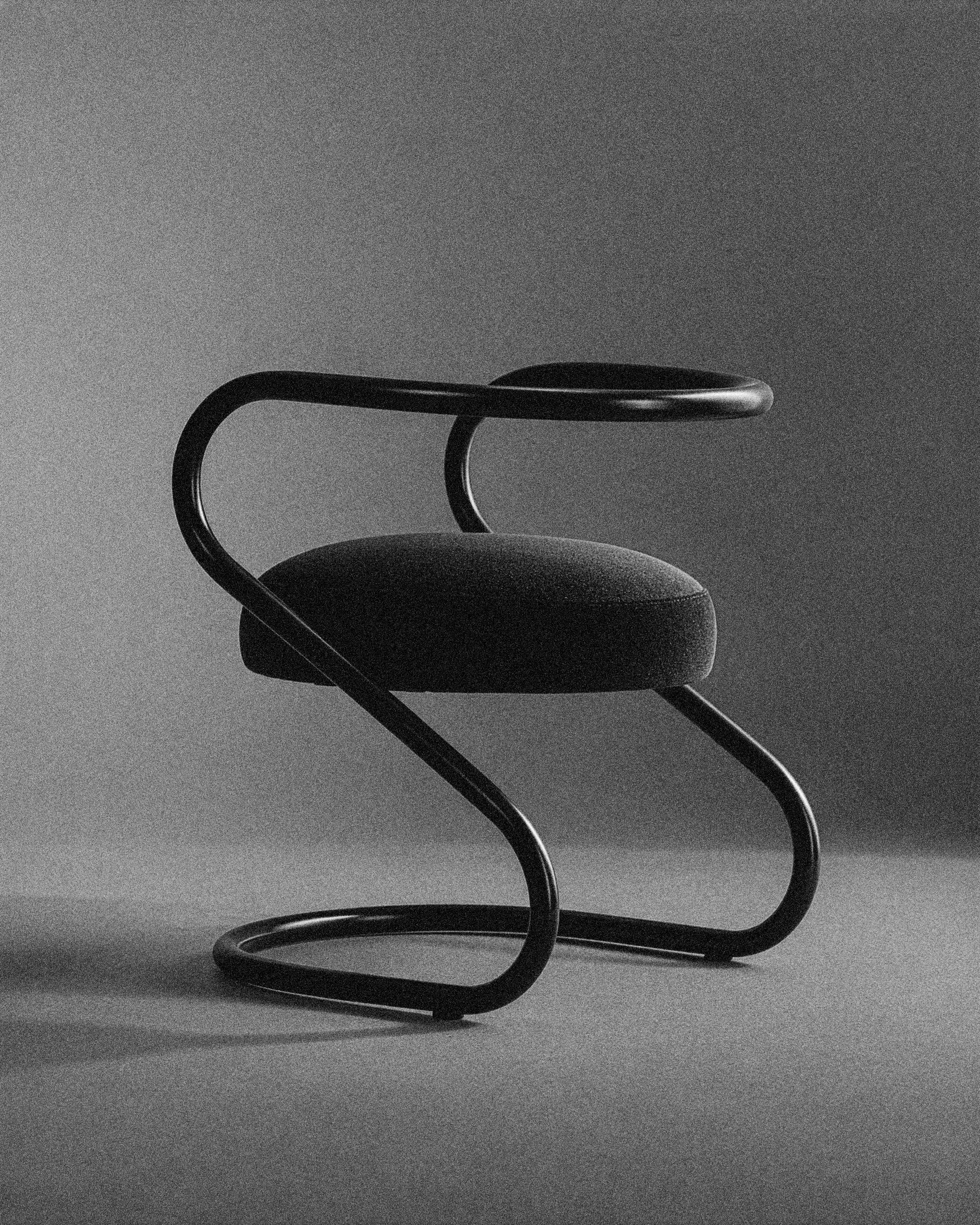 Silla S de MONSALVO, con estructura de acero tubular curvado y asiento tapizado negro, fotografiada sobre un fondo oscuro.