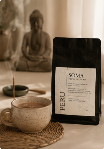 SOMA Premium Kakao Peru Packung neben einer Kakaotasse und glimmendem Räucherstäbchen vor einer verschwommenen Buddha-Statue.