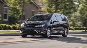A black minivan driving on a suburban street with trees and houses in the background.