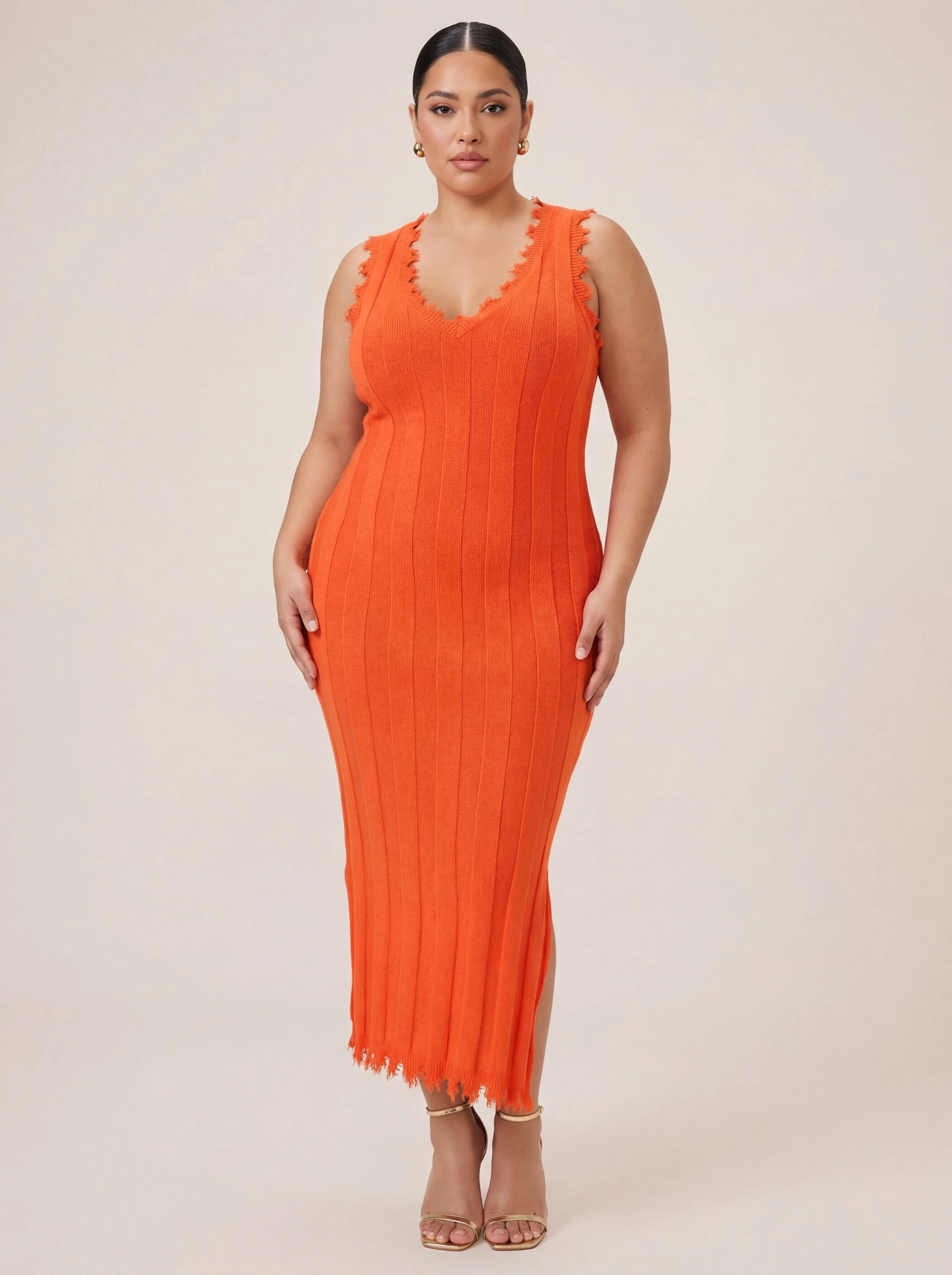 A woman wearing an orange sleeveless, ribbed knit maxi dress with a frayed hem and V-neckline, standing against a neutral background.