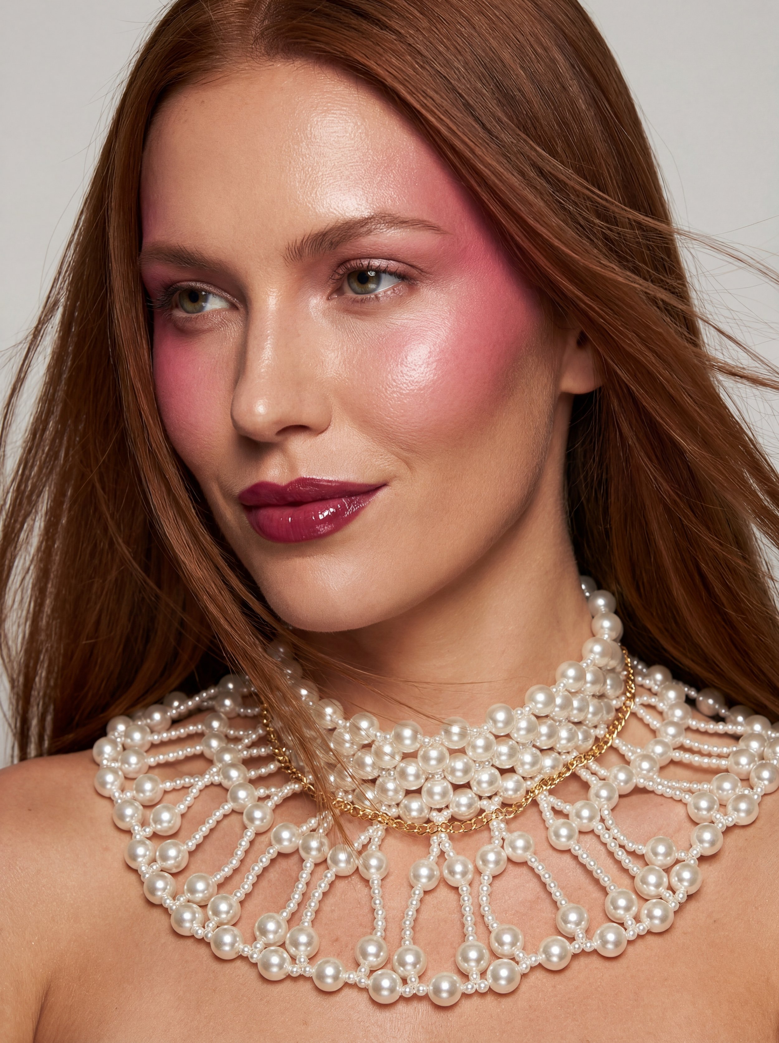 A woman with red hair wearing multiple pearl necklaces and pink makeup.