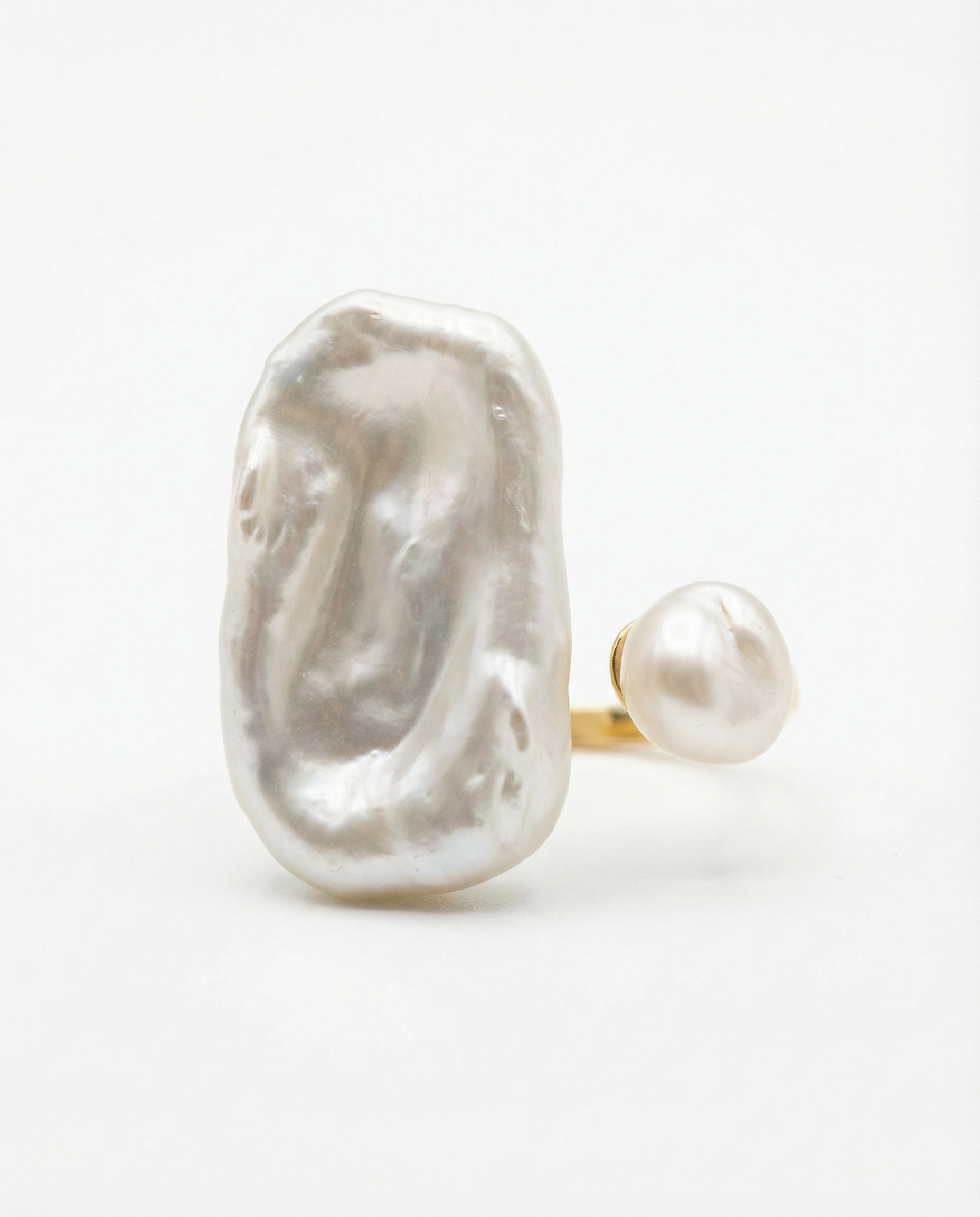 Close-up of a large, irregularly shaped white pearl with a shiny, smooth surface, mounted on a ring with a thin gold band, against a plain white background. created by idk agency