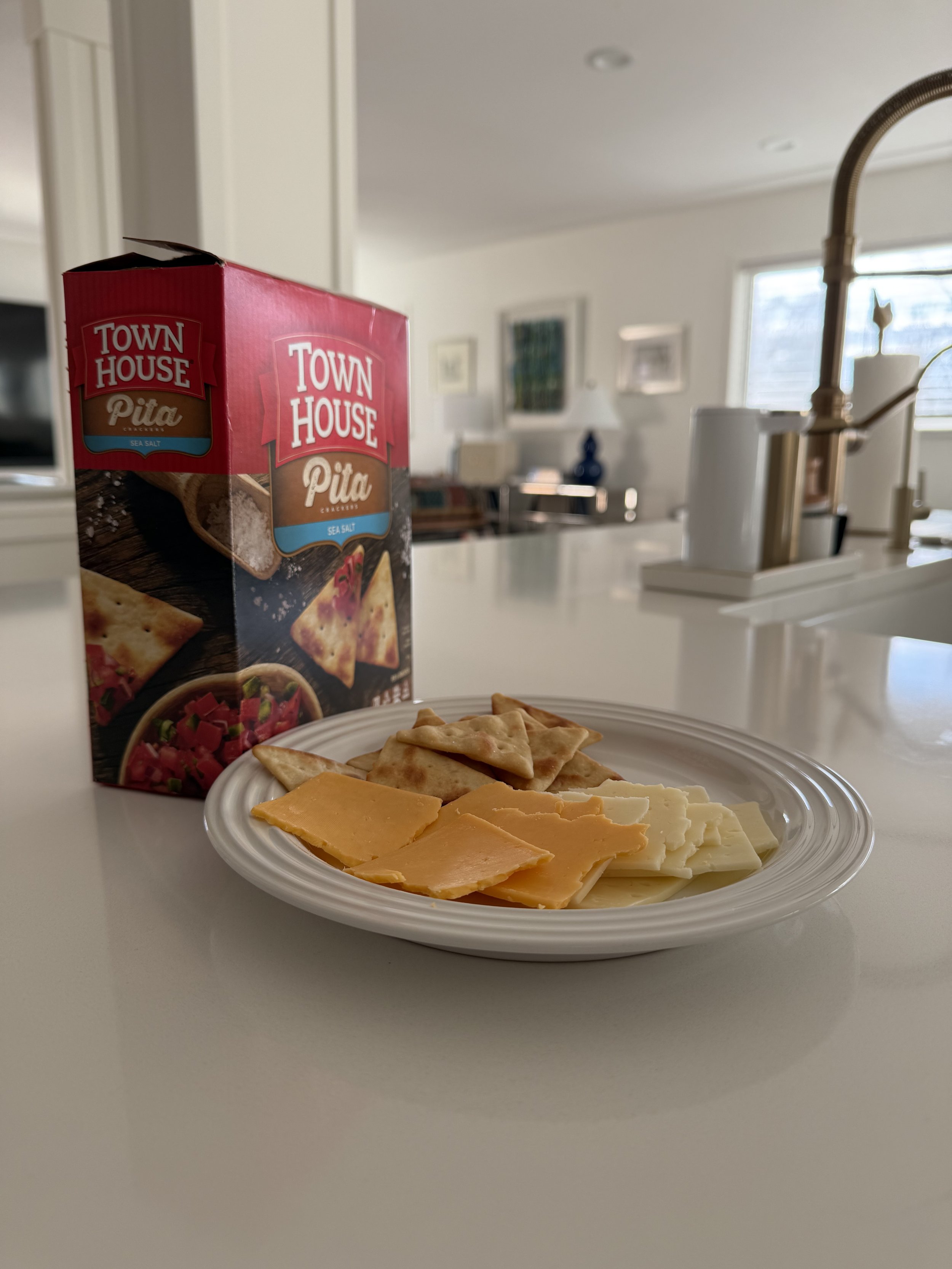Plate of sliced cheese and crackers on a kitchen counter, representing a simple, low-effort meal.