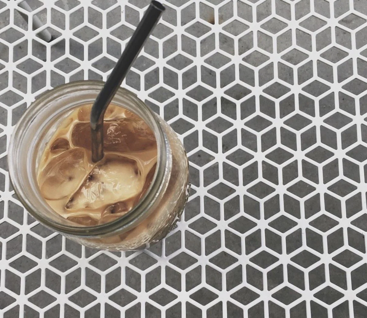 Top-down view of iced coffee with a straw in a glass jar on a patterned table.