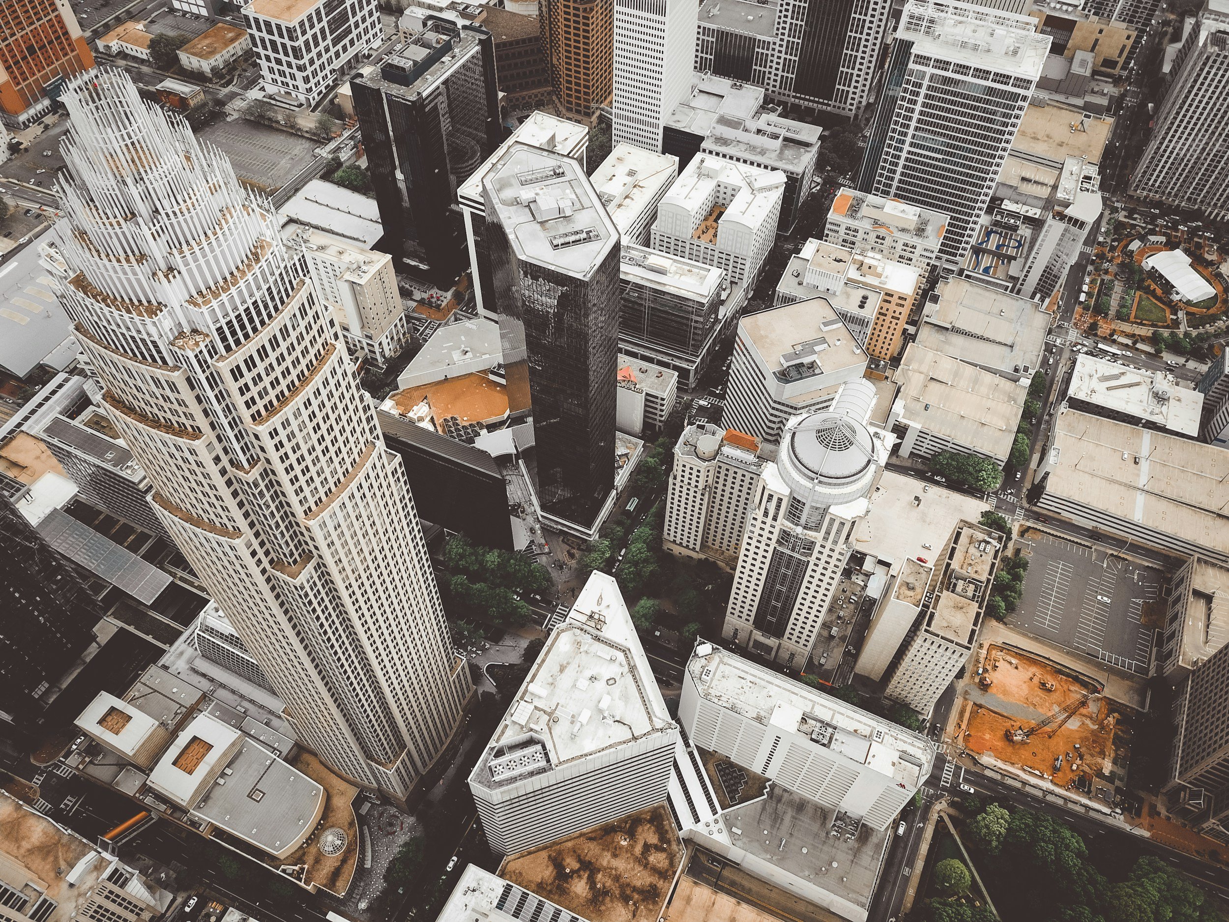 Aerial view of a dense city block with tall skyscrapers, streets, and some rooftops with construction or maintenance equipment.