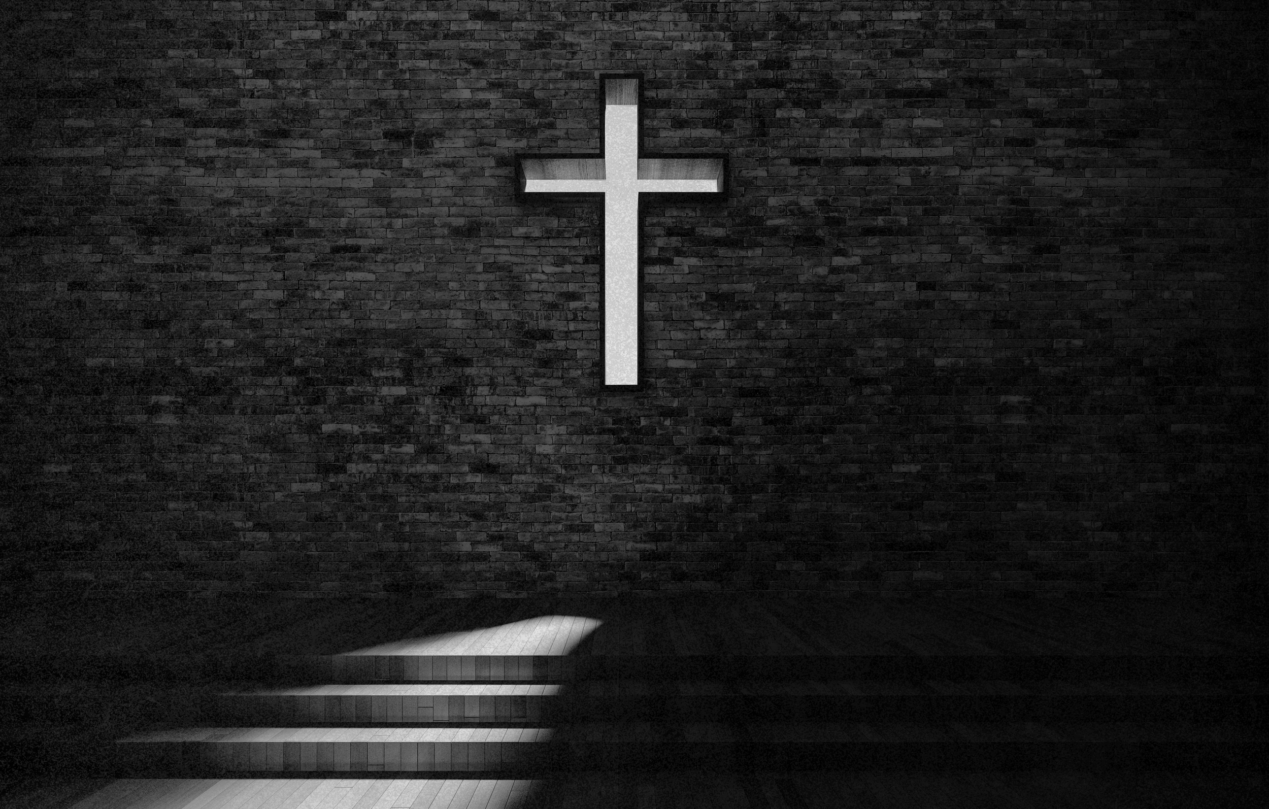 A white illuminated cross on a dark brick wall, with stairs below leading upward into darkness.