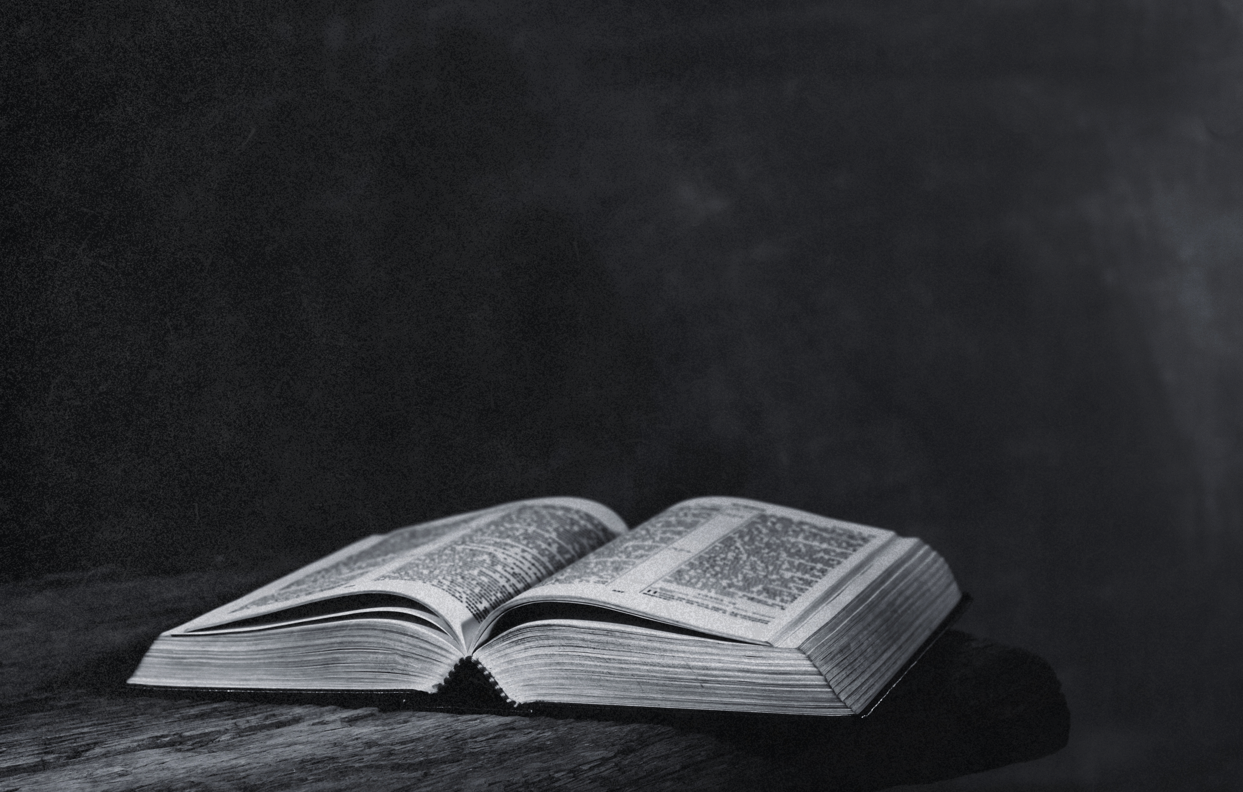 An open book with intricate black-and-white text and designs on a dark surface, with a dark background.