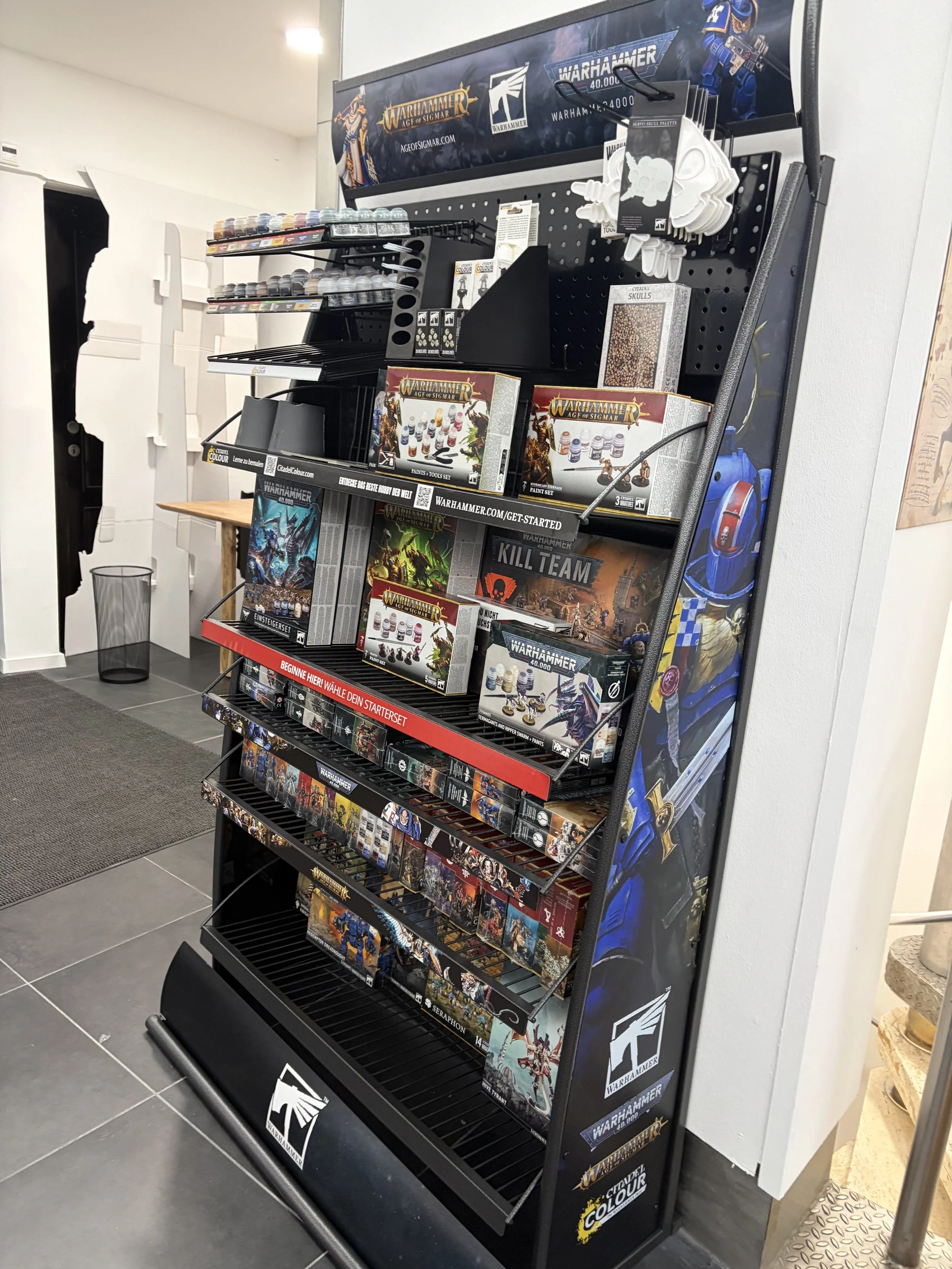 Regal mit Tabletop-Spielen und Malsets für Warhammer, in einem Geschäft aufgestellt.