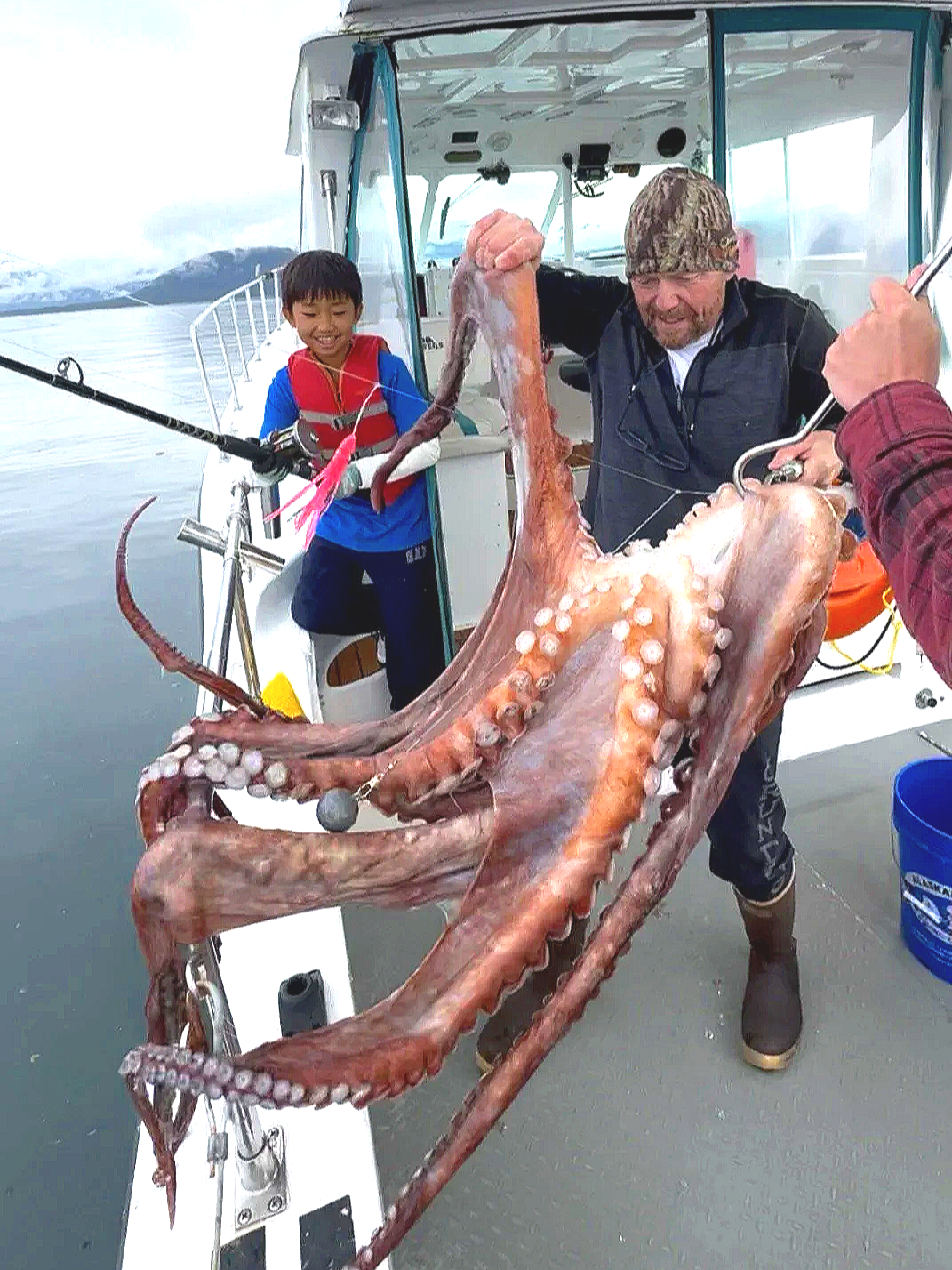 Two people on a boat holding a large octopus.