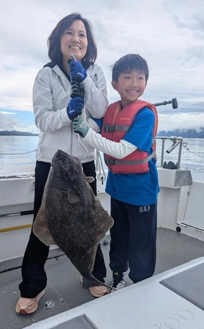 A woman and a boy on a boat, holding a large fish they caught.