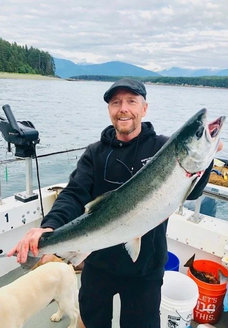 Man holding large Salmo on a boat with water and mountains in the background.