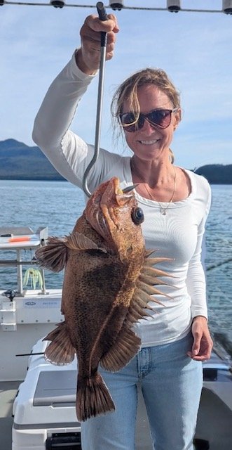 Woman holding a large fish on a boat with water and hills in the background