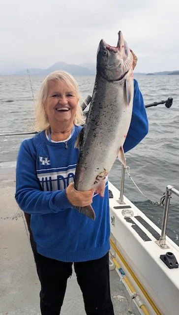 Smiling woman holding large fish on a boat with water and distant islands in the background.
