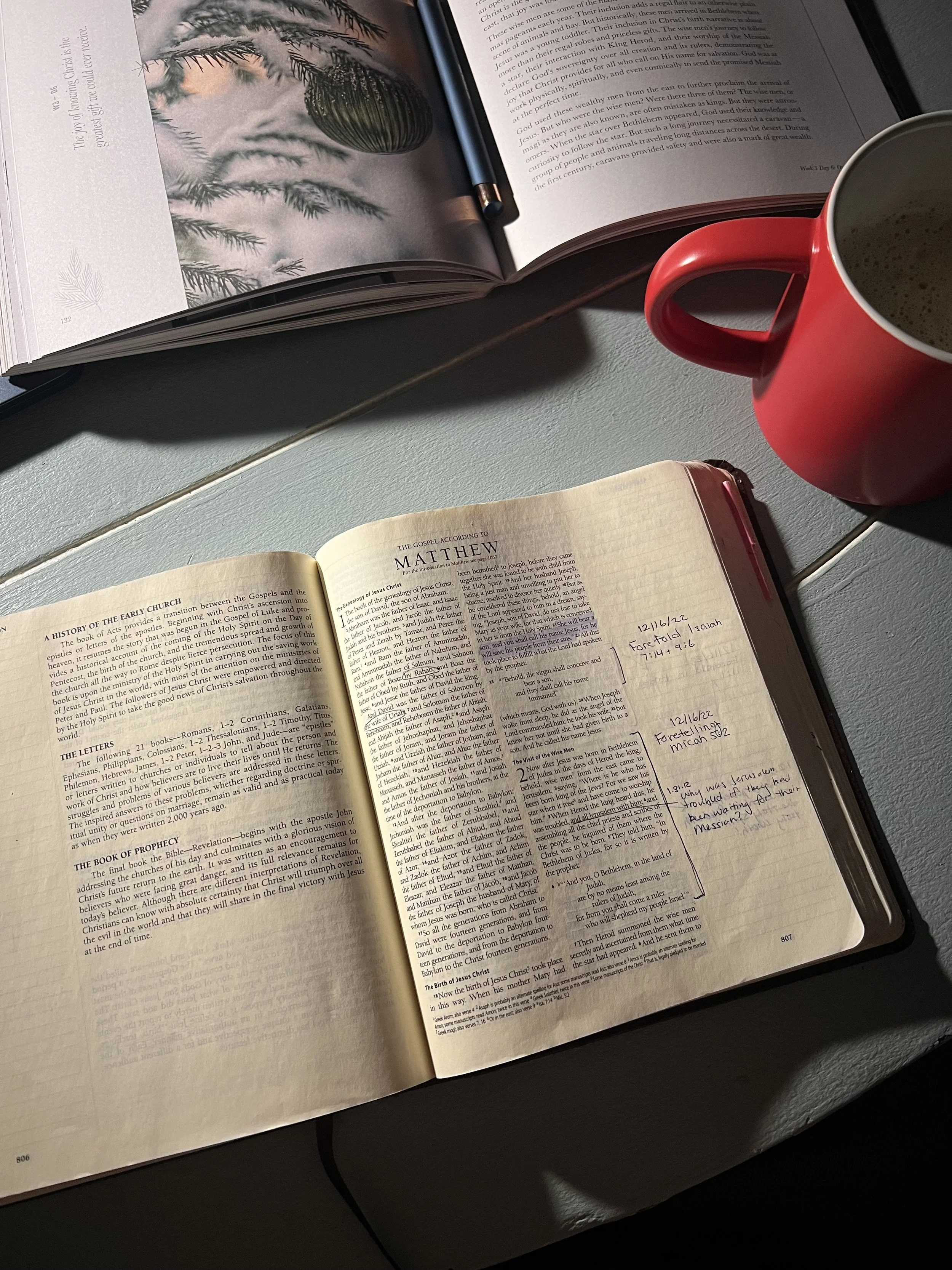 Open Bible with handwritten notes, red coffee mug, and open magazine on a light-colored table.
