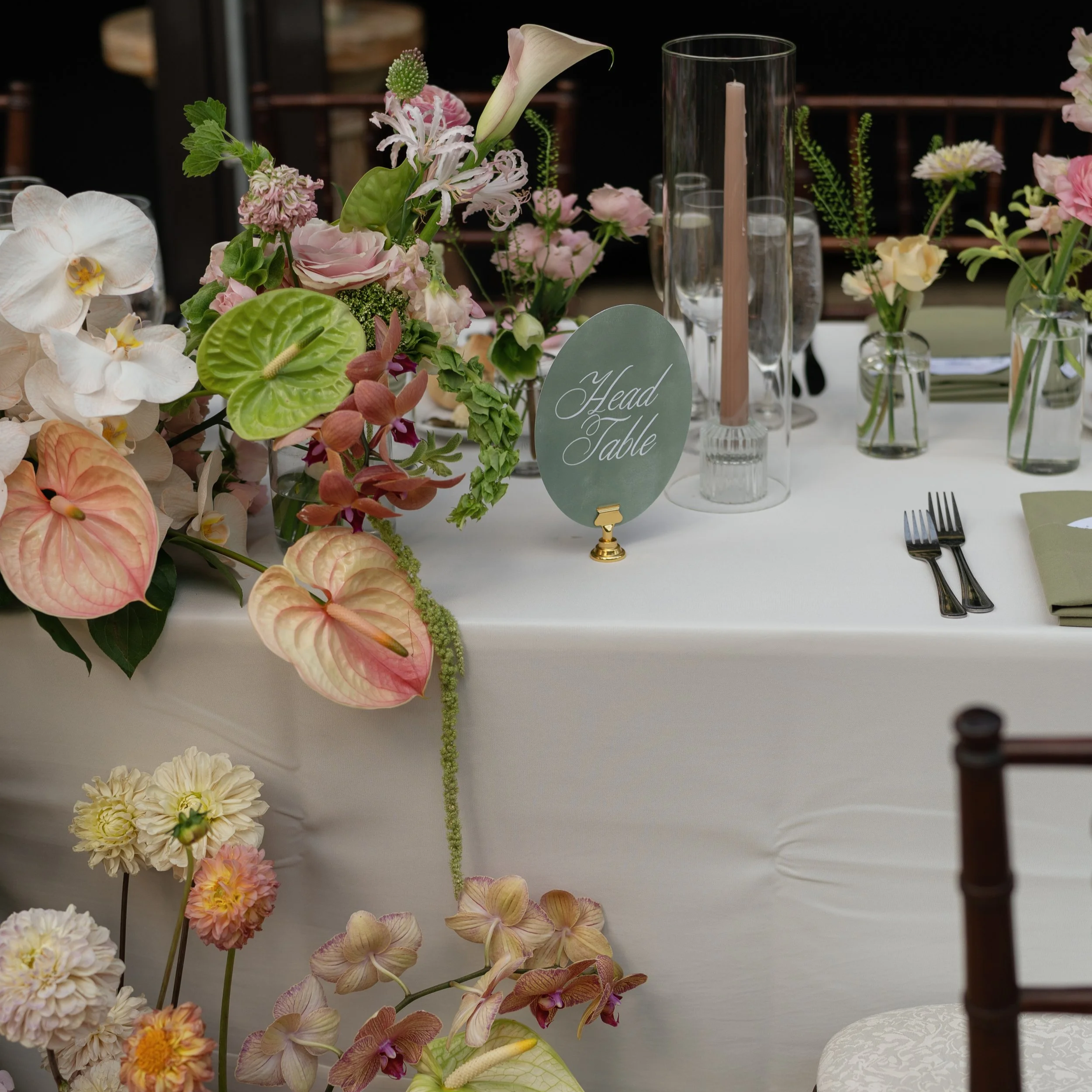 Elegant table setting with floral centerpiece, candles, glassware, and utensils, designated as 'Head Table' with a sign.