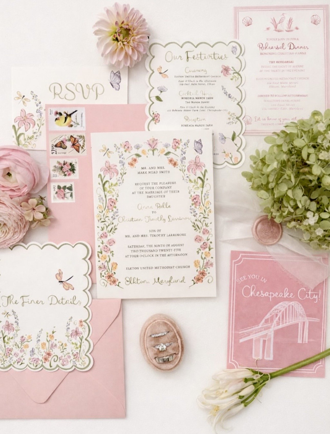 Wedding invitation suite with floral decorations, including RSVP card, ceremony and reception details, a pink envelope with floral design, and small flowers and greenery, along with a pink ring box containing rings and a pink 