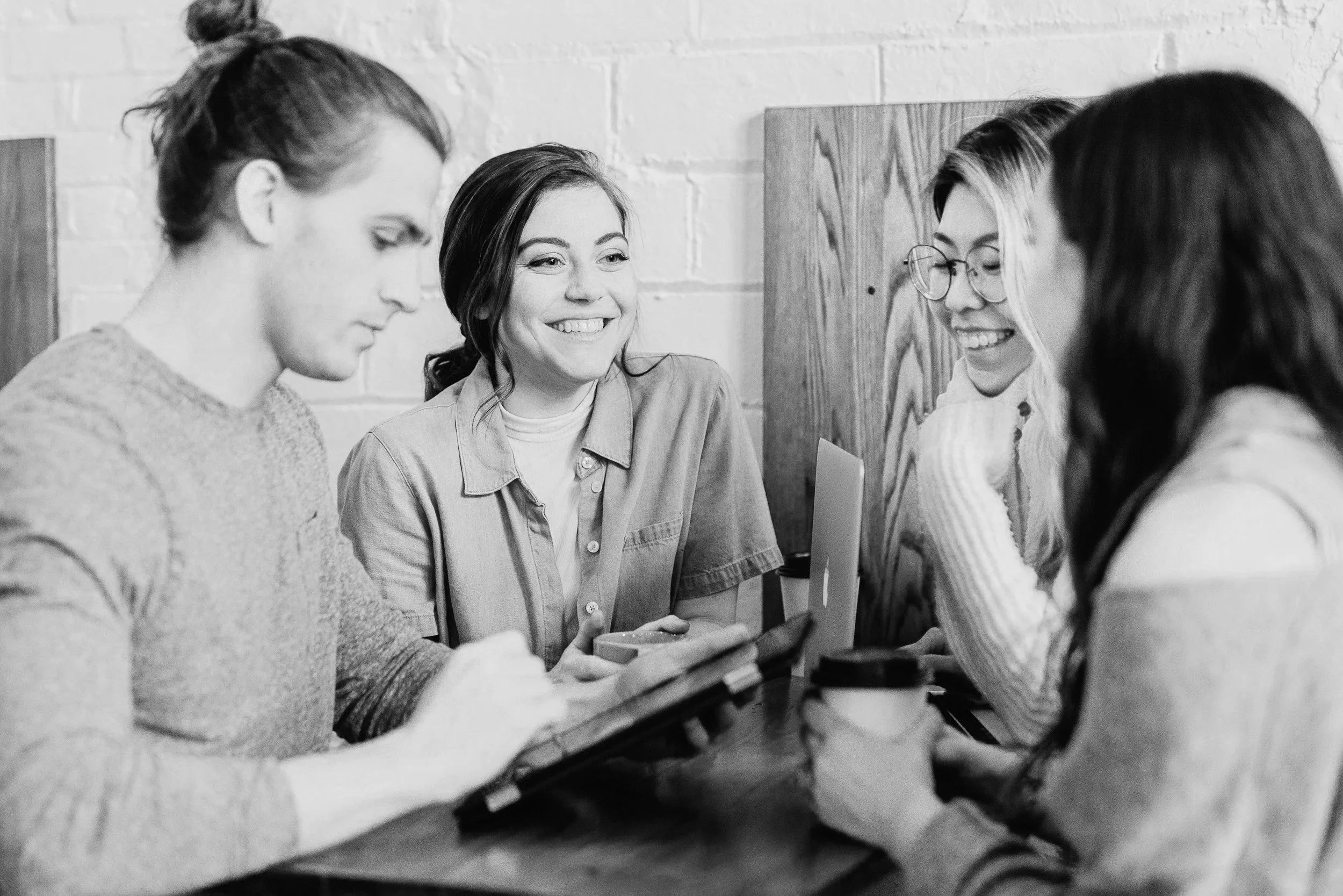 Four women sitting at a table in a cafe, working together and smiling, with a brick wall and wood paneling in the background. Membership Communities can sell event tickets on Squarespace with Eventually.