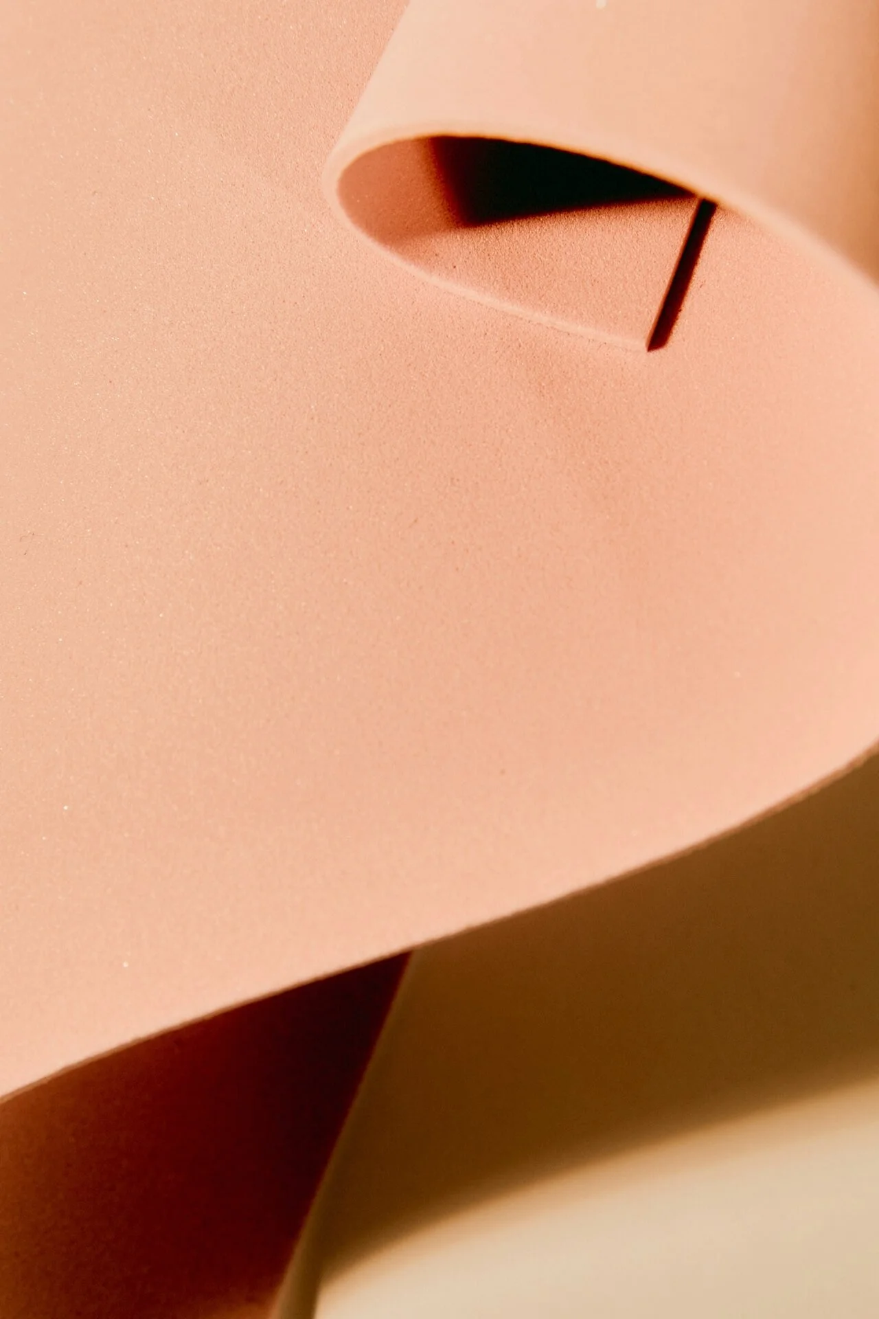 Close-up of a pink paper sheet with rounded edges and a black slit, partly rolled.