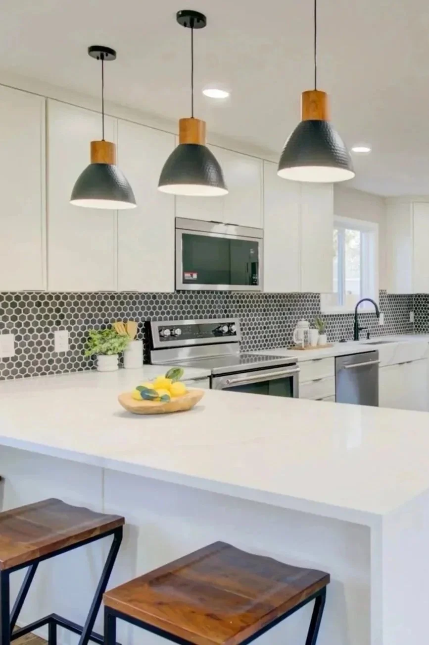 Modern kitchen with white cabinets, black hexagon tile backsplash, stainless steel appliances, white countertops, pendant lights, and bar stools.