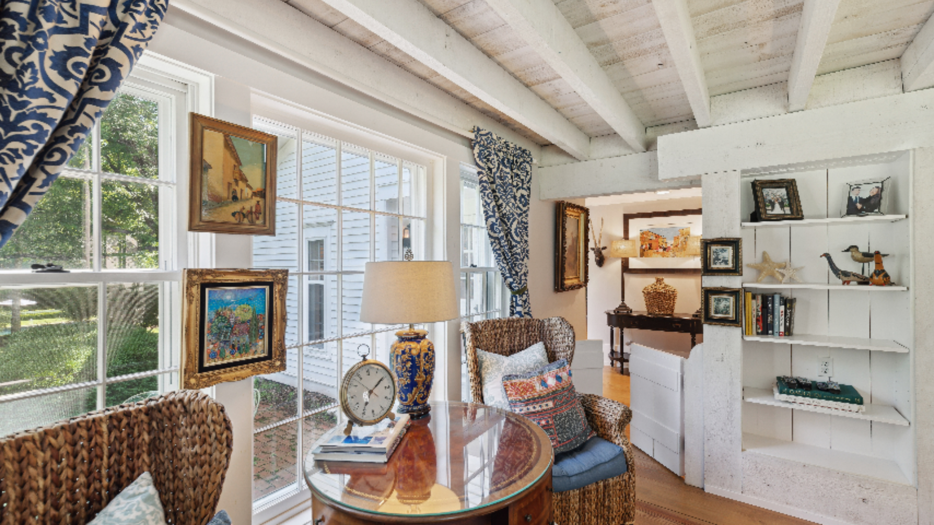 French Country Sunroom - Whitewashed exposed beams and reclaimed wood ceiling set the tone for this charming retreat, layered with woven wicker chairs, indigo block-print draperies, and a gallery of original artwork. A custom built-in bookcase and an