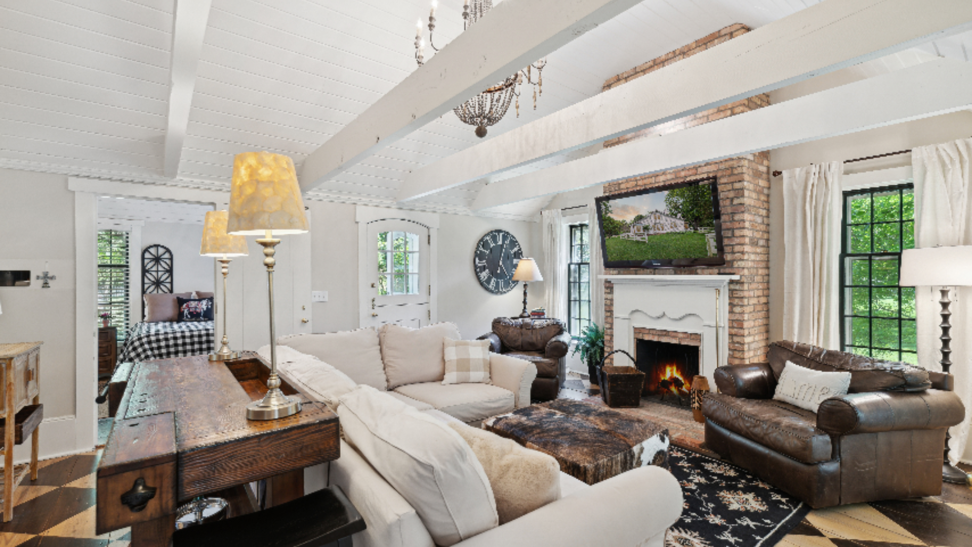 Vaulted Great Room - Soaring whitewashed beams and a brick fireplace bring rustic character to this comfortable living space, where soft linen sofas play against rich leather seating for a lived-in, layered look. A checkerboard-painted floor, cowhide