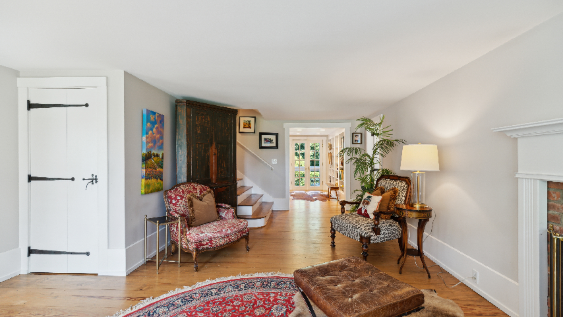 Sitting Room with Sightlines - This gracious room offers a long view straight through to the entry beyond, with a mix of upholstered antique chairs, a leather bench, and layered rugs creating a relaxed, collected feel. A wood-burning fireplace anchor