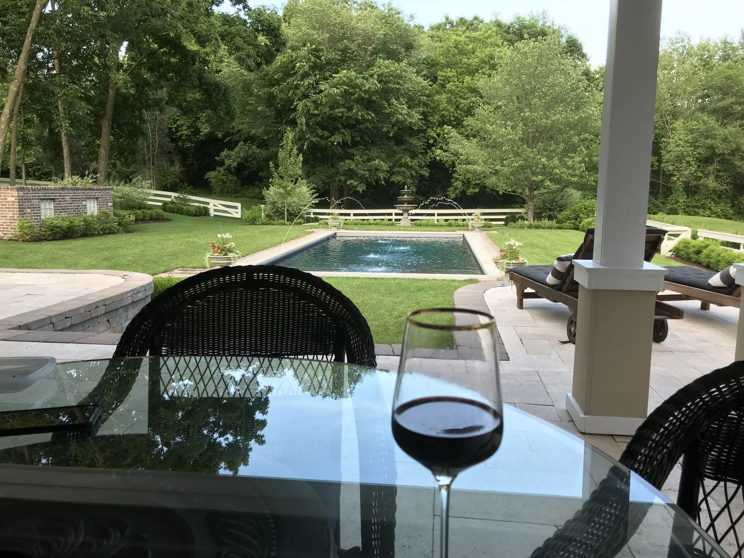 After: A luxurious outdoor space with a travertine-tiled veranda, steps leading to lush grass, a stunning pool, all completed by MichaelAngela Properties. 