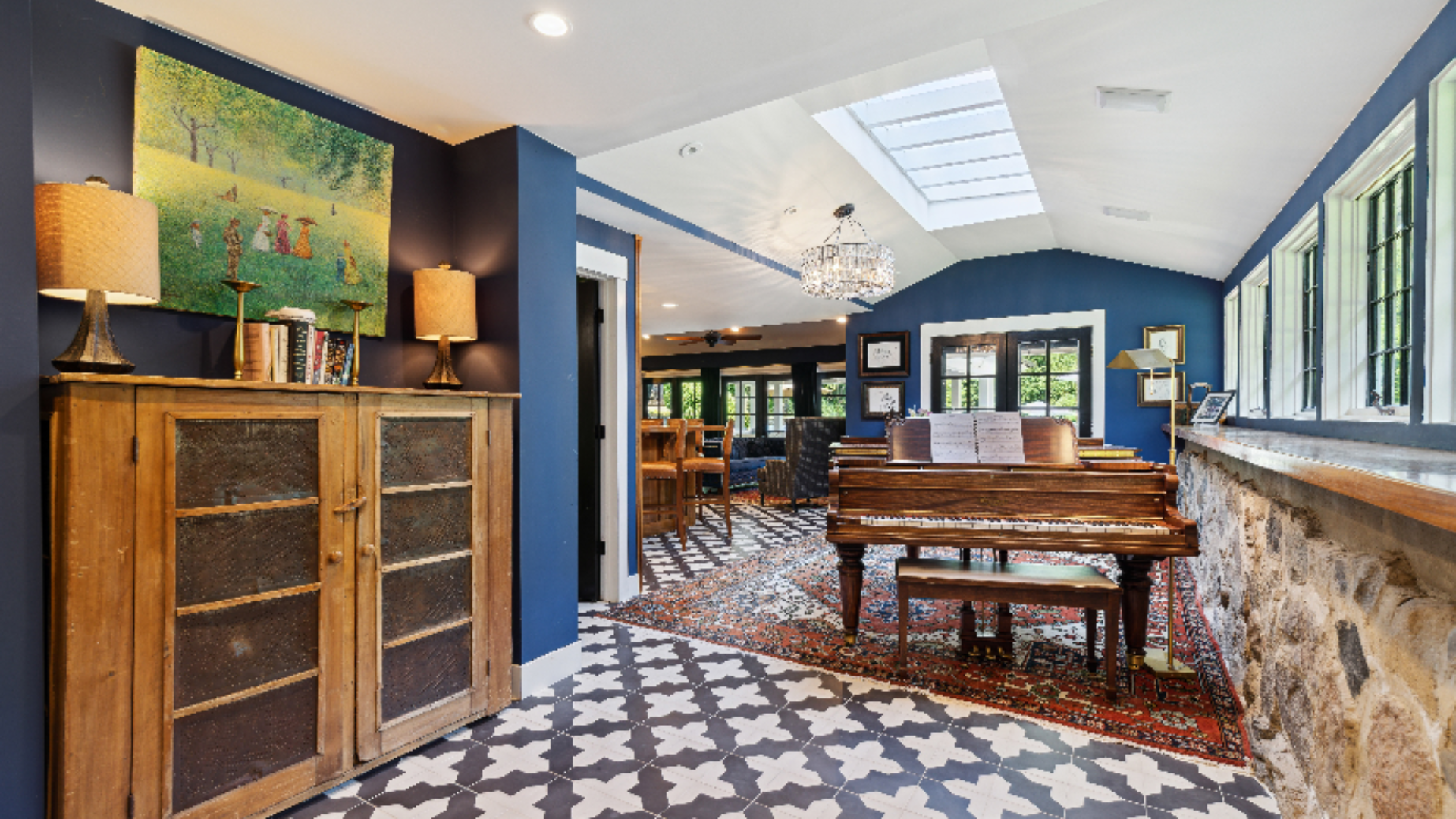 Music Room with Bold Blue Walls - Deep navy walls create a dramatic backdrop for this vaulted music room, anchored by a vintage baby grand piano and warmed by natural fieldstone. A graphic patterned rug resting on imported Nicaraguan cement tile and 