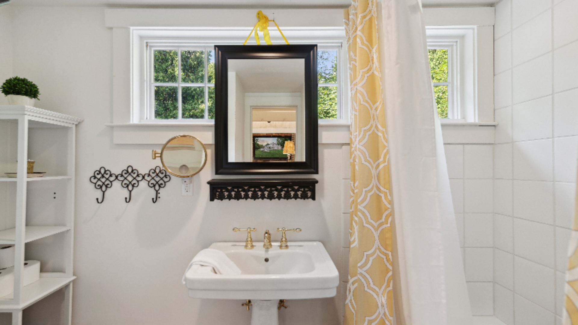 Cheerful Cottage Bath - A crisp white pedestal sink with polished brass fixtures pairs beautifully with a sunny yellow patterned shower curtain for a fresh, cottage-style feel. A black-framed mirror, white shelving, and playful wall hooks keep the sp