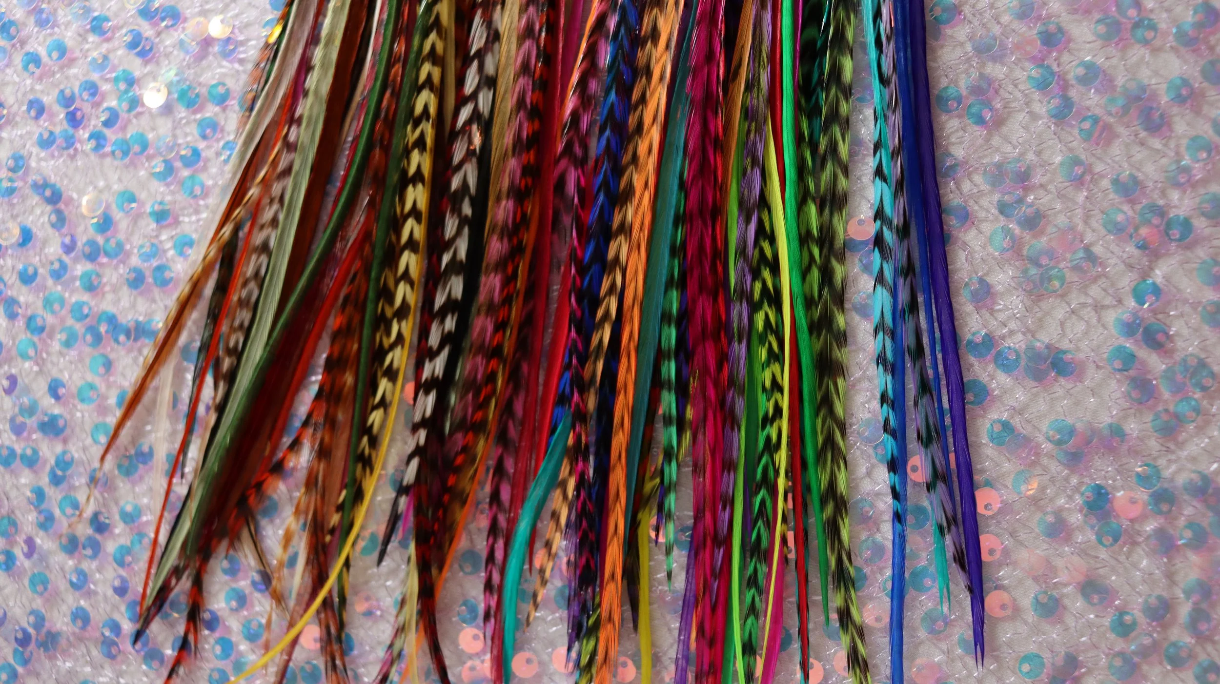 colorful and neutral hair feathers for hair extensions and festivals on a purple sparkly background