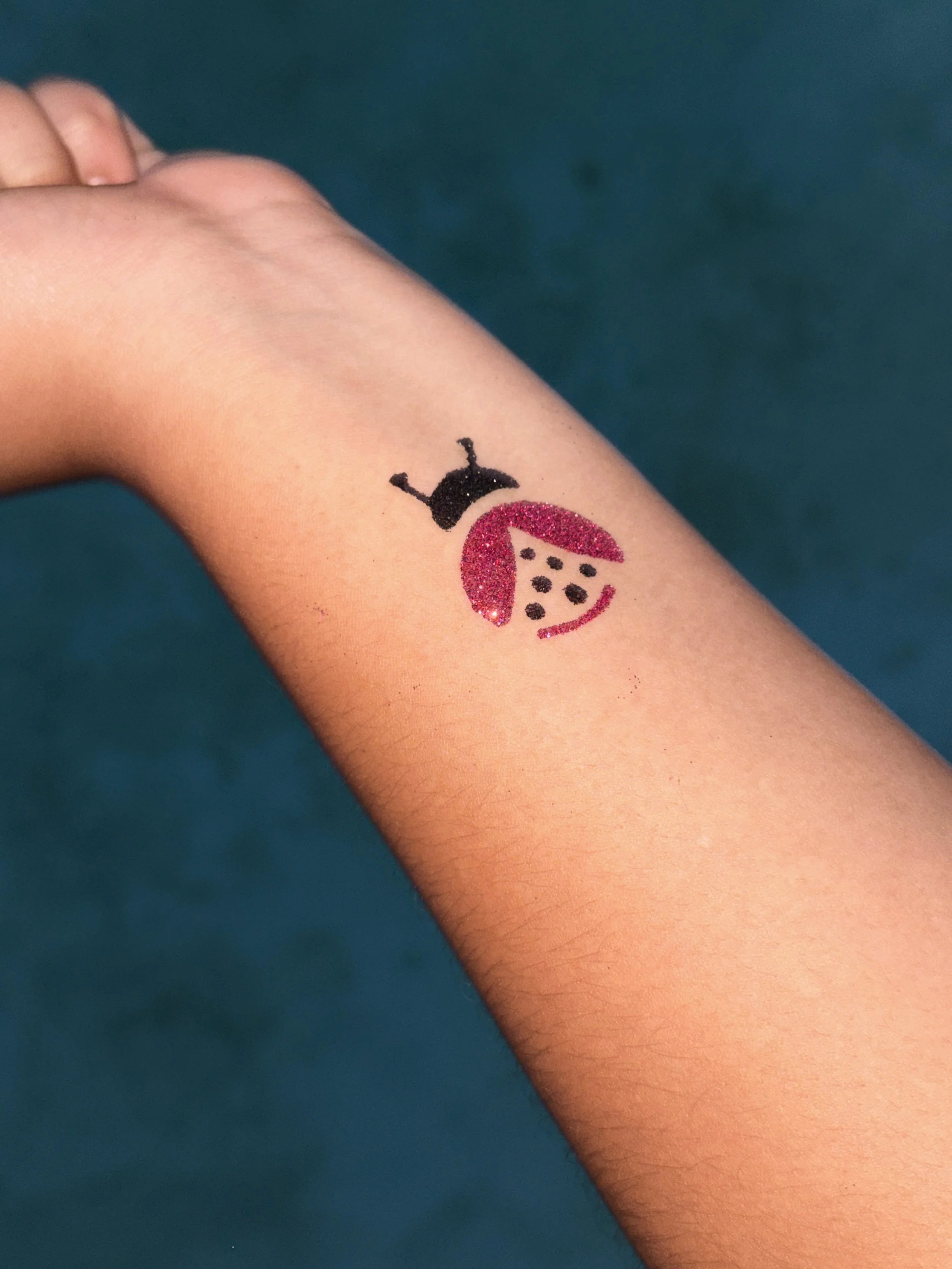 pink and black glitter tattoo ladybug on arm
