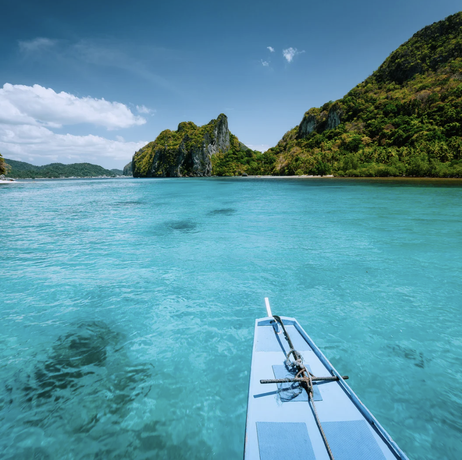 Vue d'une mer turquoise avec une ile montagneuse en arrière-plan et un bateau à l'avant.