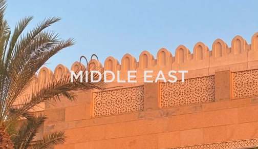 Middle Eastern desert wall with inscription and palm tree under a clear blue sky, reflecting international hospitality markets served by DC Global Talent.