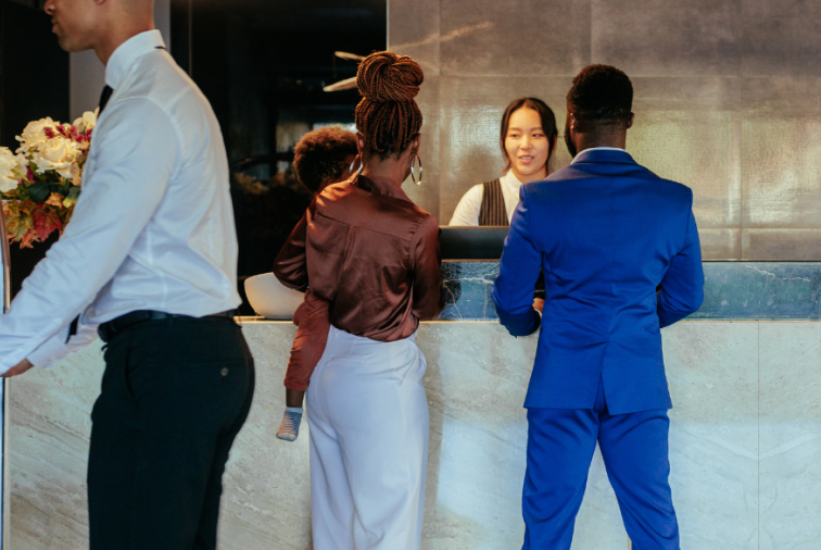 People at a hotel check-in counter, engaging with a receptionist behind the desk.