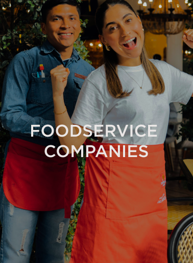 Two smiling food service workers wearing aprons in a warmly lit restaurant with greenery and “Foodservice Companies” text overlay, representing the hospitality employers served by DC Global Talent recruitment specialists.