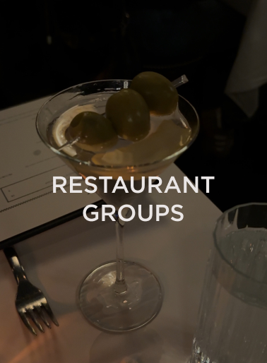 Cocktail glass with green olives on skewers on a restaurant table, representing the hospitality and restaurant industry served by DC Global Talent recruitment specialists.