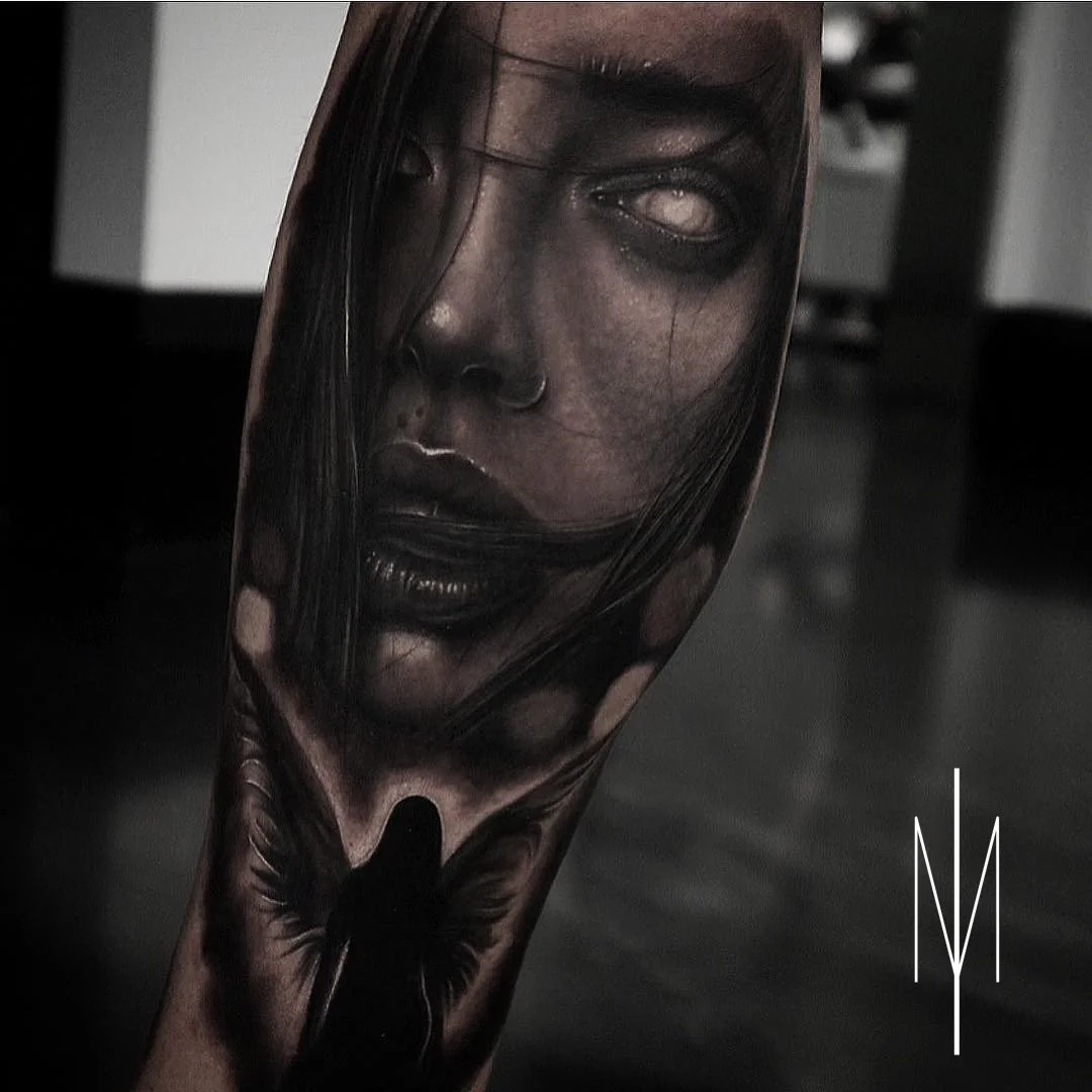 Tattoo of a woman's realistic face with long dark hair on a person's arm.