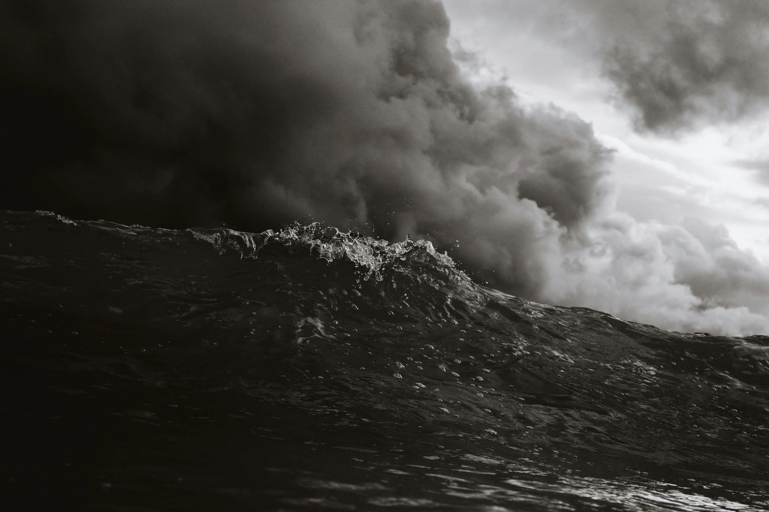 Black and white photo of rough ocean waves with dark storm clouds overhead.