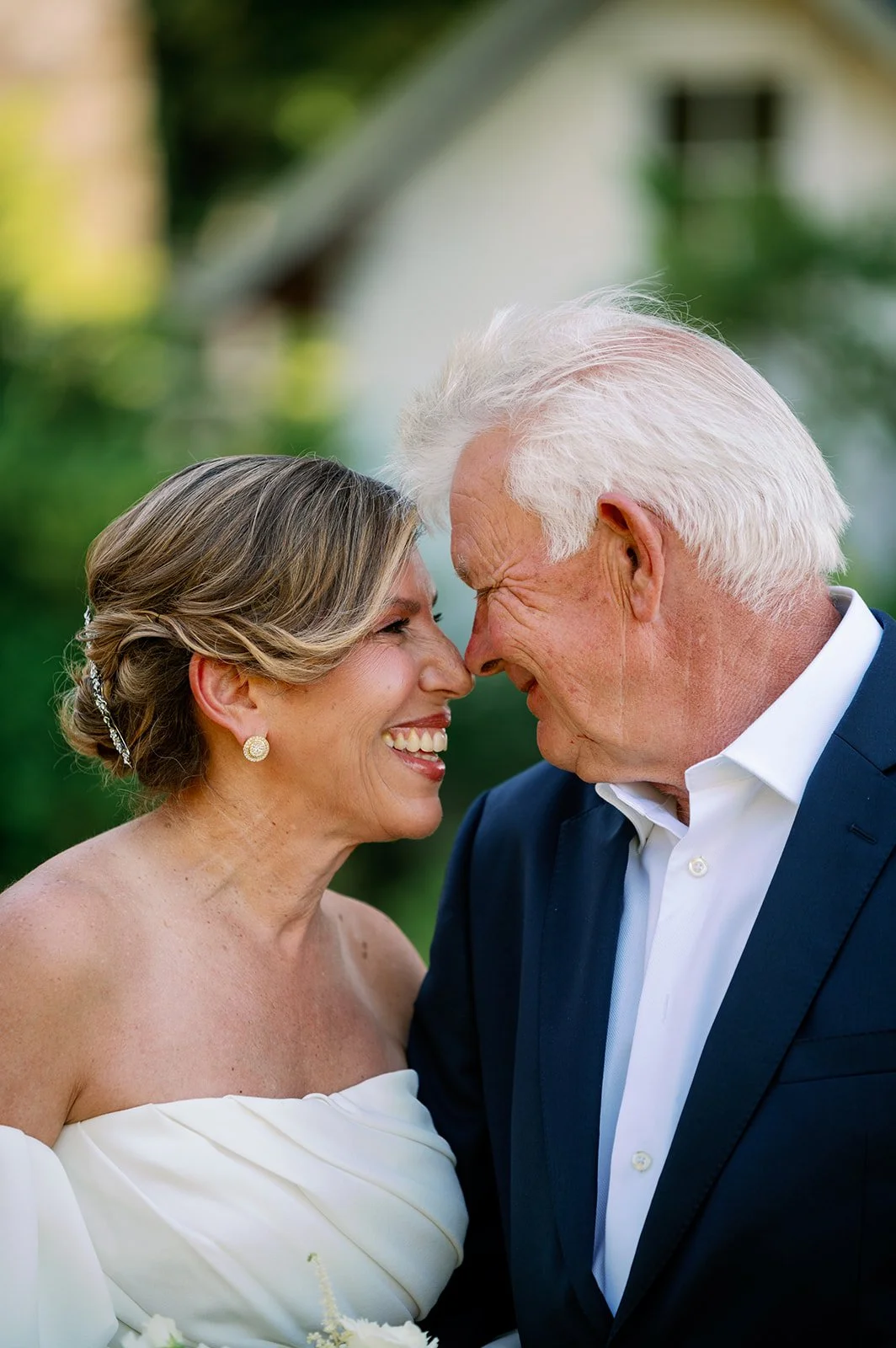 Close-up of a smiling bride and an elderly groom touching foreheads outdoors.