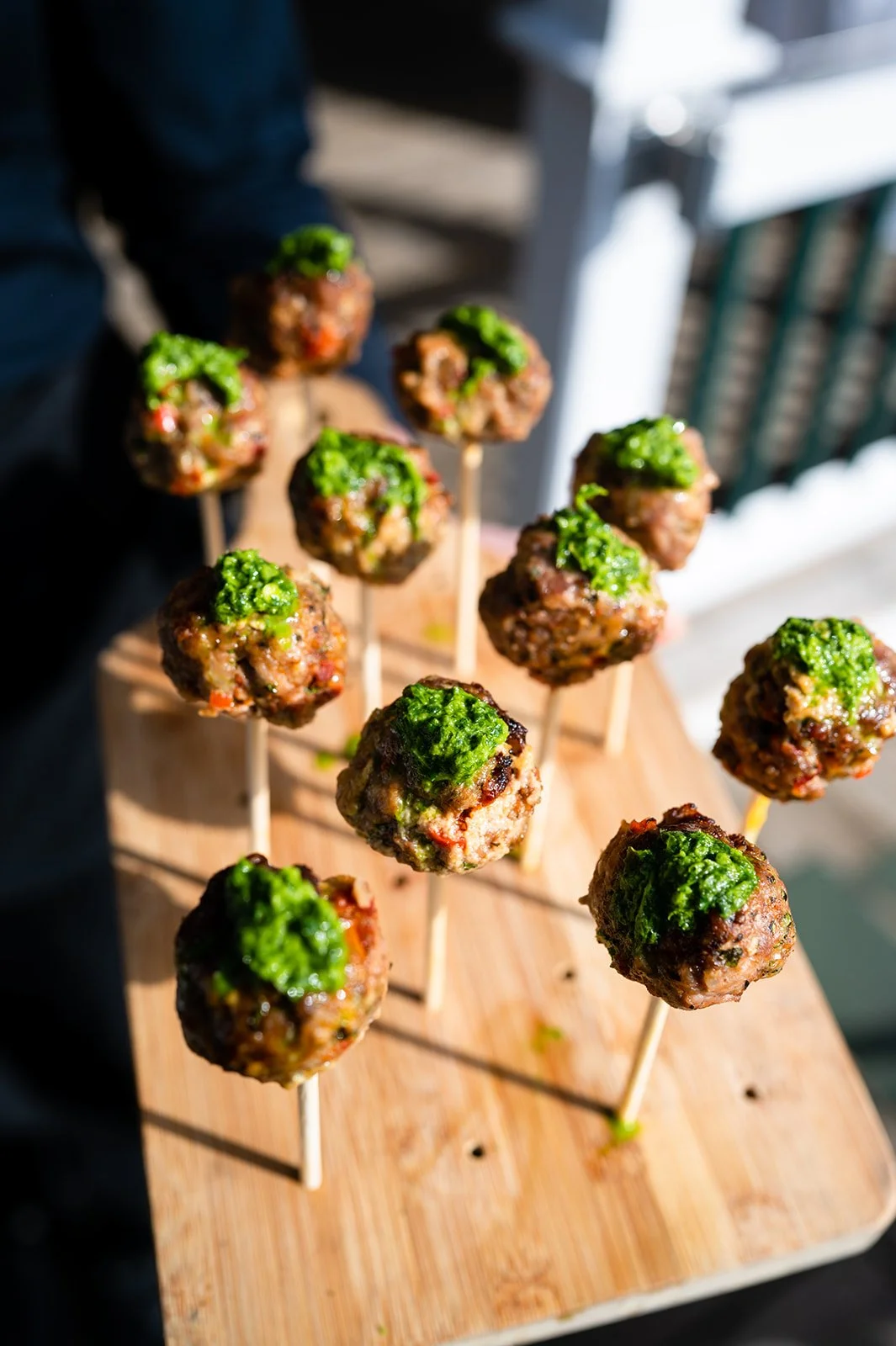 Meatballs on sticks with green garnish served on a wooden board.